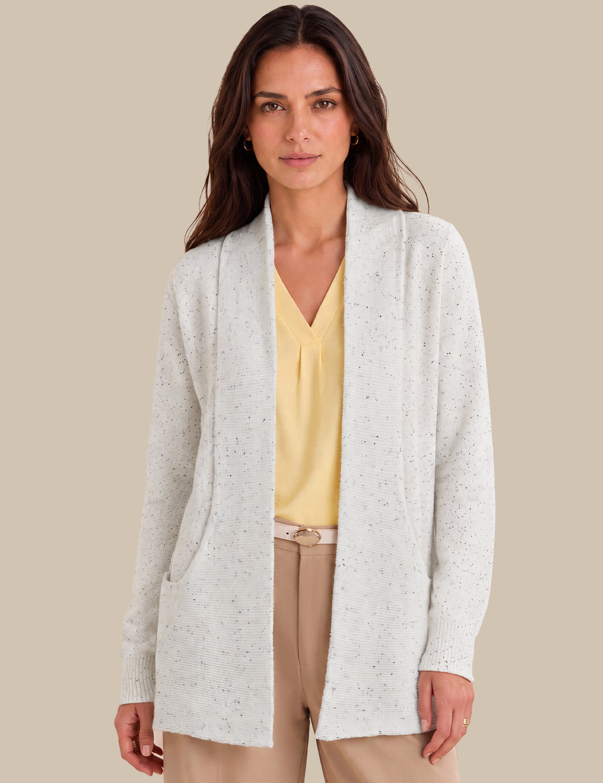 A woman modeling a lvory open-front cardigan with subtle speckled texture, worn over a yellow blouse and beige pants, against a solid beige background.