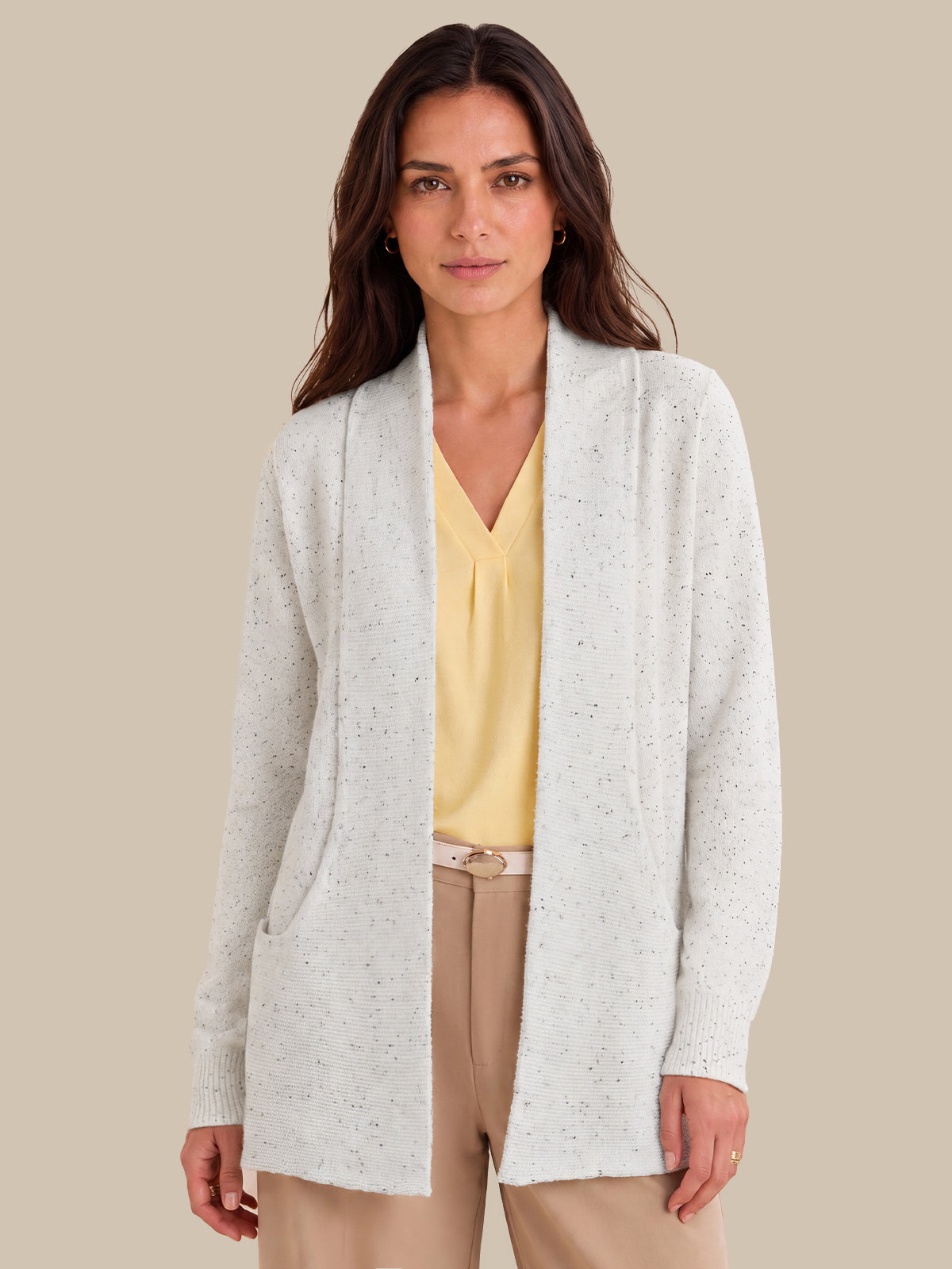 A woman modeling a lvory open-front cardigan with subtle speckled texture, worn over a yellow blouse and beige pants, against a solid beige background.