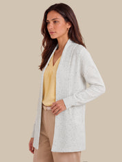 A woman wearing a lvory speckled open-front cardigan over a yellow top and beige pants, posed against a solid beige background.