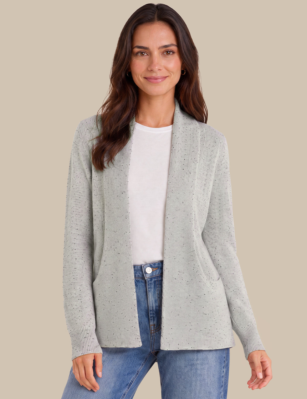 A woman modeling a light gray open-front knit cardigan over a white top and blue jeans, set against a solid beige background.
