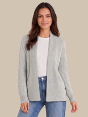 A woman modeling a light gray open-front knit cardigan over a white top and blue jeans, set against a solid beige background.