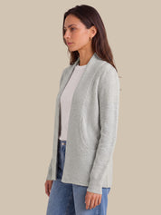 A woman wearing a light gray open-front cardigan over a white top and blue jeans, shown in profile against a solid beige background.