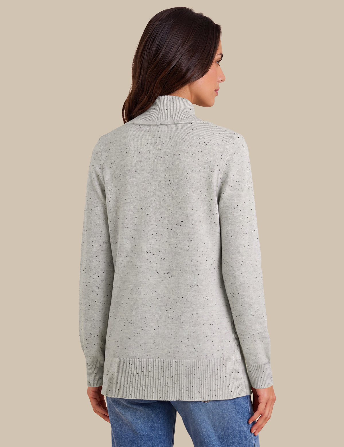 A woman shown from the back wearing a light heather gray knit sweater with a mock neck, paired with blue jeans, against a solid beige background.