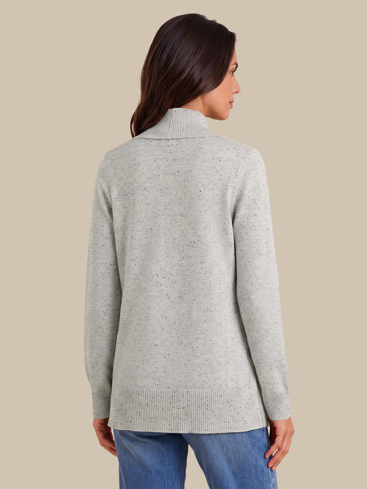 A woman shown from the back wearing a light heather gray knit sweater with a mock neck, paired with blue jeans, against a solid beige background.