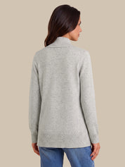 A woman shown from the back wearing a light heather gray knit sweater with a mock neck, paired with blue jeans, against a solid beige background.