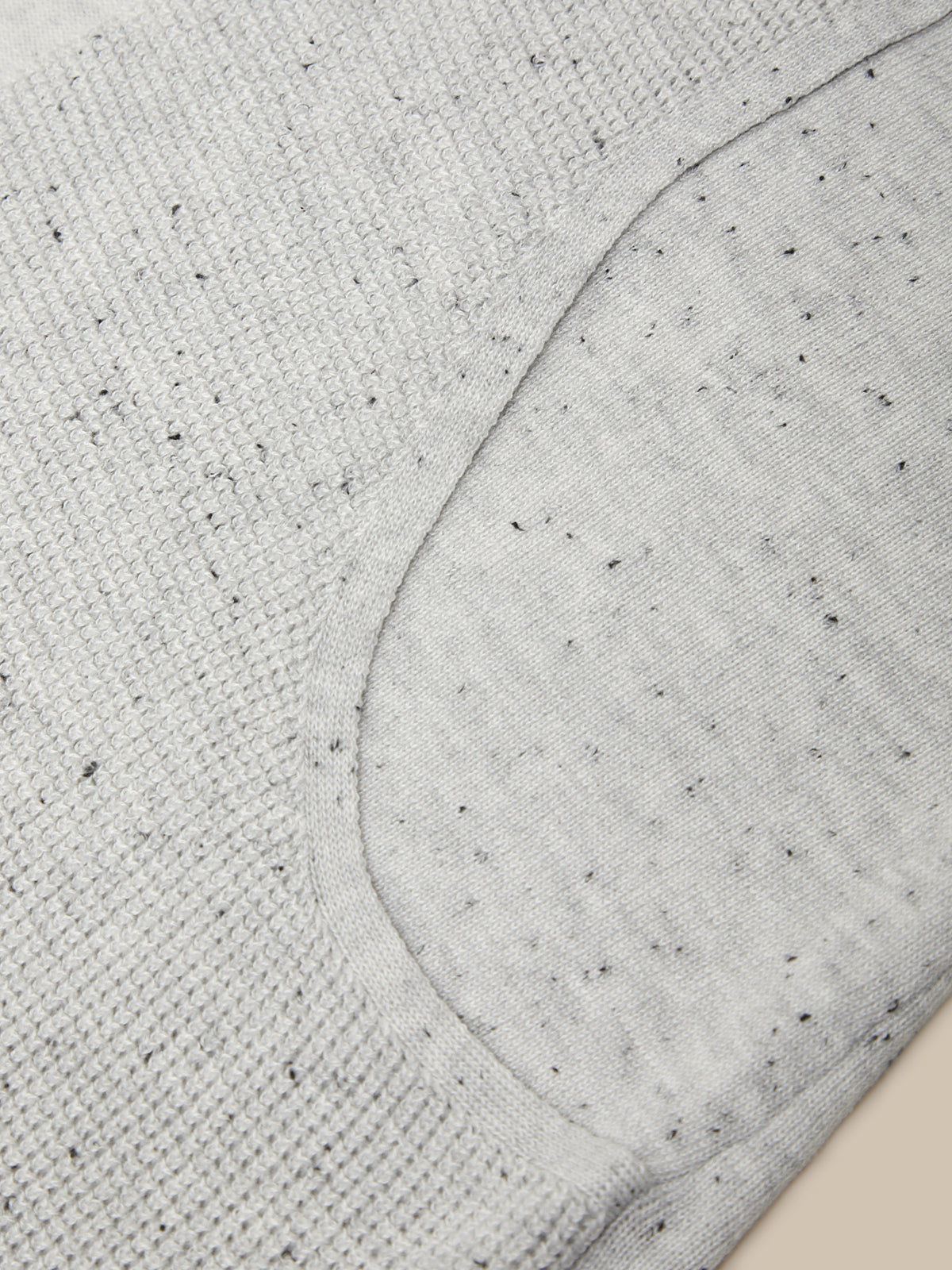Close-up of a light gray heather knit fabric with small black flecks, showing a curved seam and ribbed texture.
