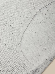 Close-up of a light gray heather knit fabric with small black flecks, showing a curved seam and ribbed texture.