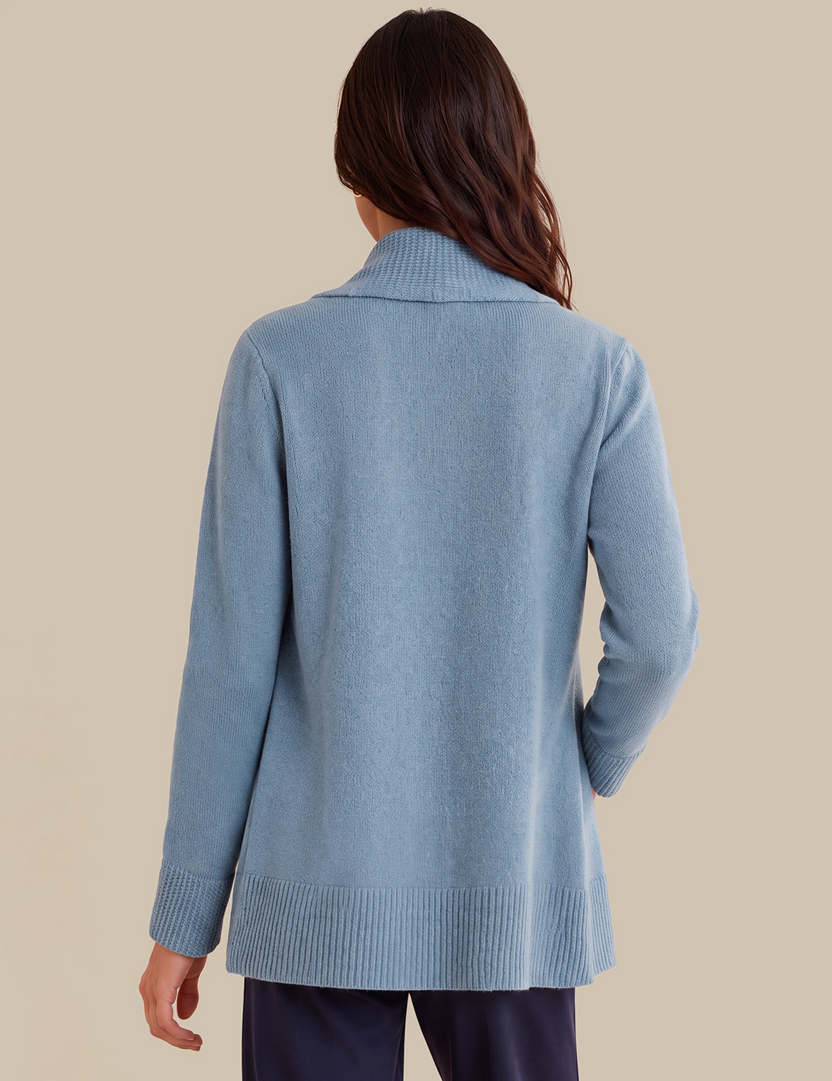 A woman viewed from the back wearing a light blue knit cardigan with a ribbed collar, cuffs, and hem, paired with dark navy pants, against a solid beige background.