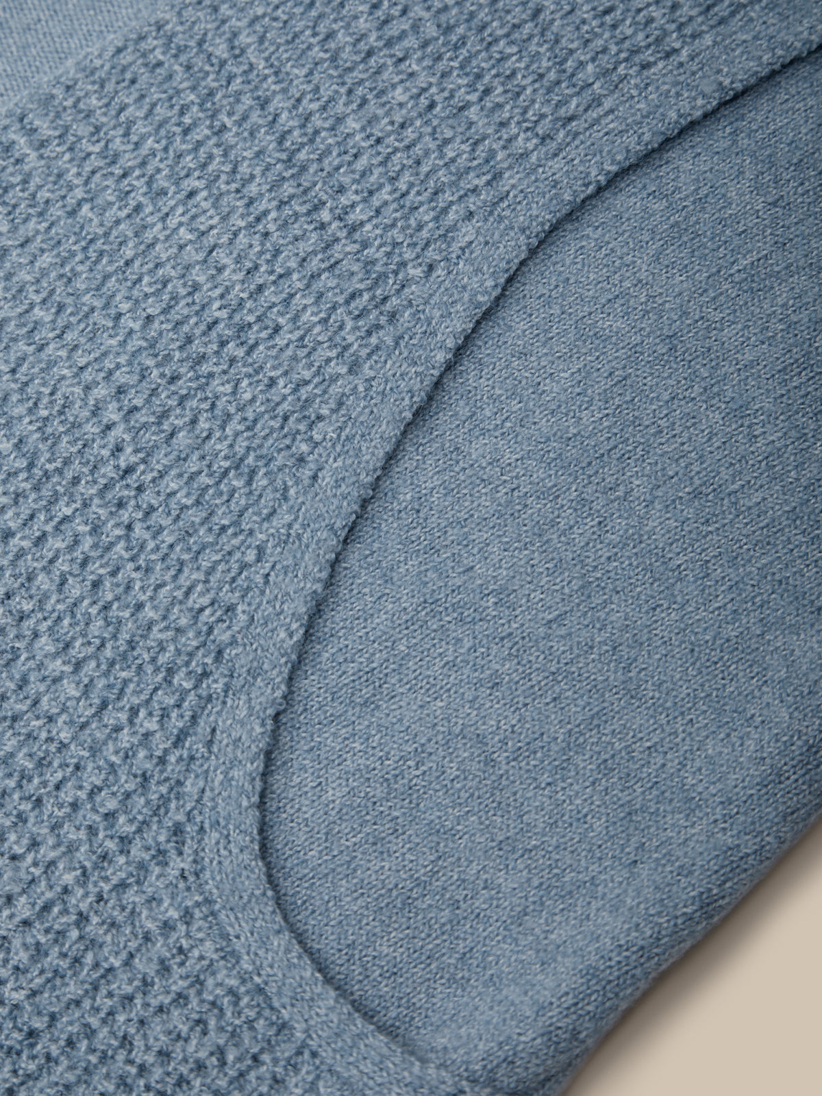 Close-up of a light blue knit garment showing a textured waffle-knit section and a smooth curved panel.