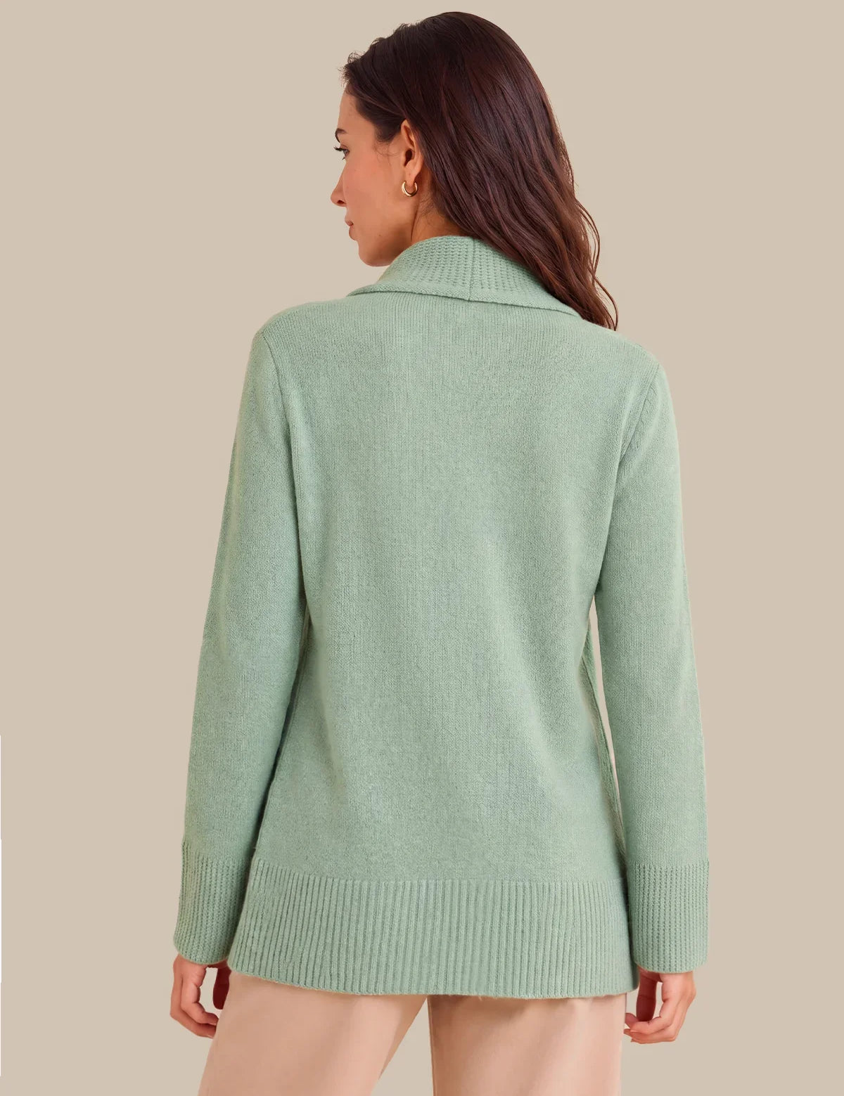 A woman shown from the back wearing a light sage green knit sweater with a wide collar and ribbed cuffs and hem, against a solid beige background.