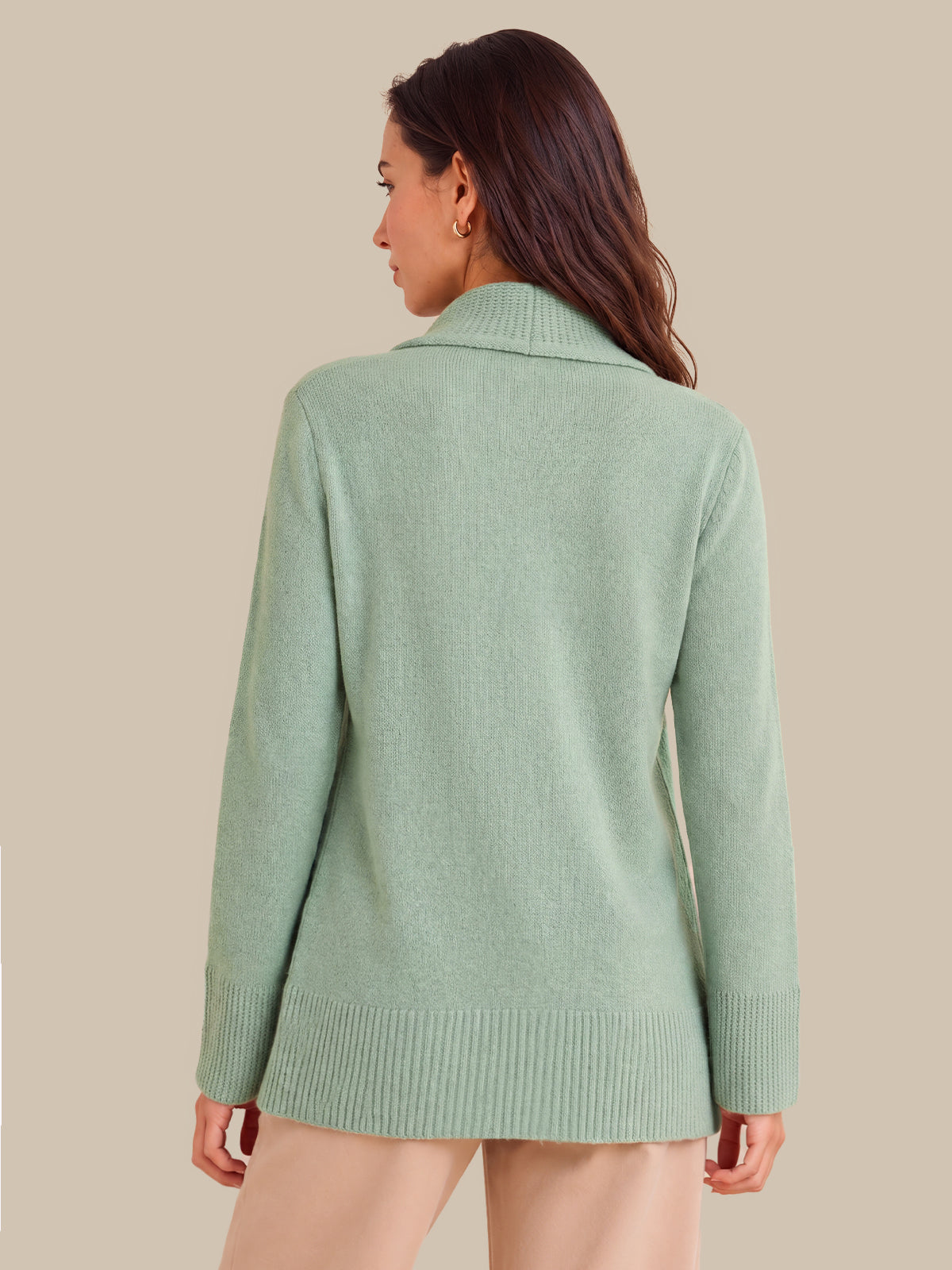 A woman shown from the back wearing a light sage green knit sweater with a wide collar and ribbed cuffs and hem, against a solid beige background.