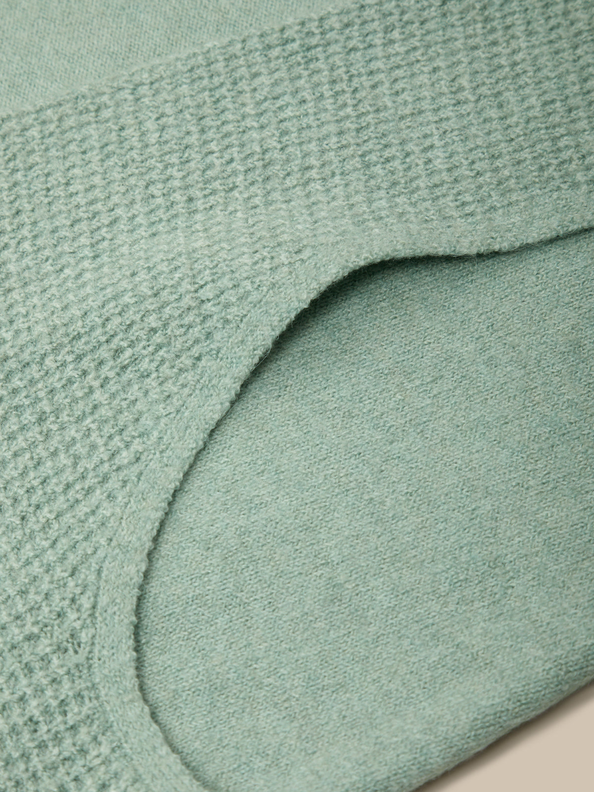 Close-up of a mint green knit garment showing the waffle-knit texture and curved neckline.