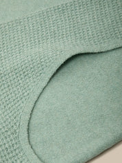 Close-up of a mint green knit garment showing the waffle-knit texture and curved neckline.