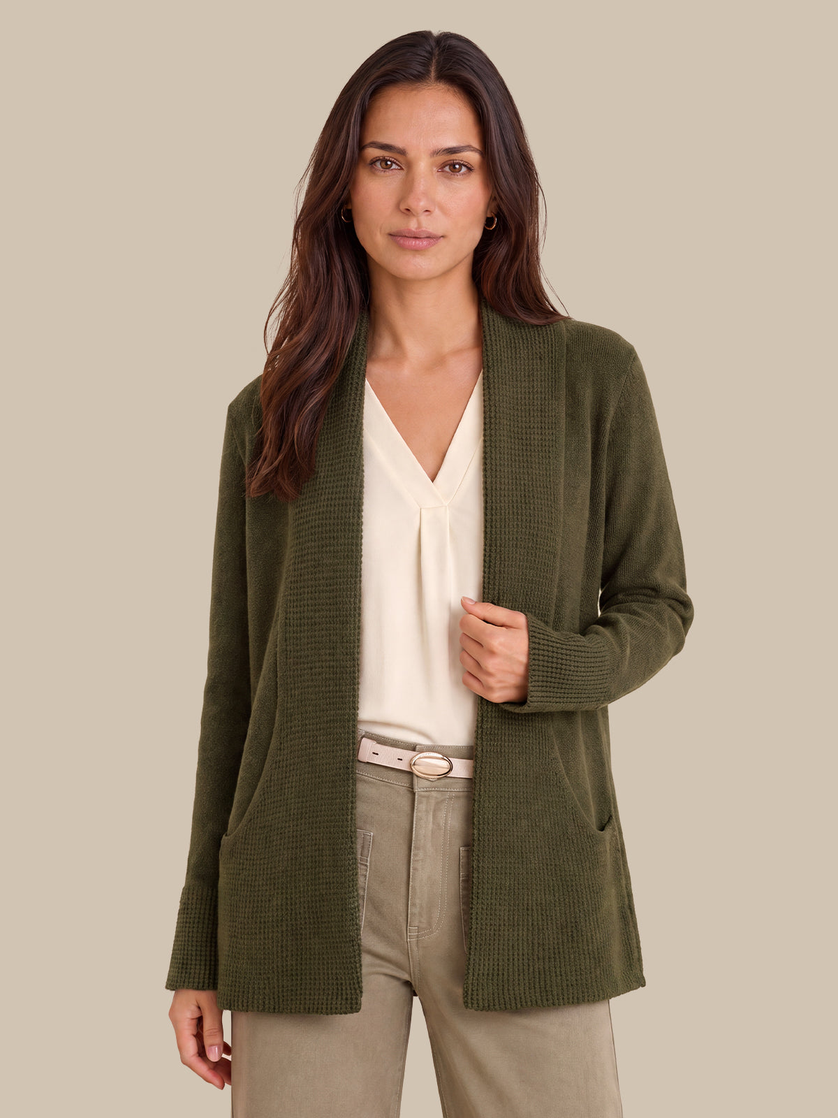 A woman modeling an olive green ribbed knit cardigan over a cream blouse and beige trousers, set against a solid beige background.