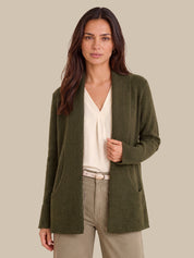 A woman modeling an olive green ribbed knit cardigan over a cream blouse and beige trousers, set against a solid beige background.