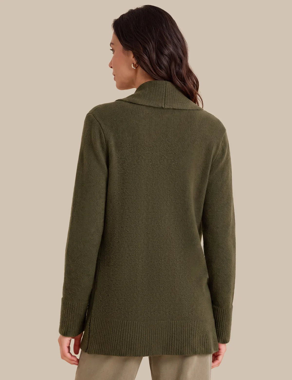 A woman shown from the back wearing an olive green knit sweater with a wide collar and ribbed cuffs and hem, paired with light beige pants, against a solid beige background.
