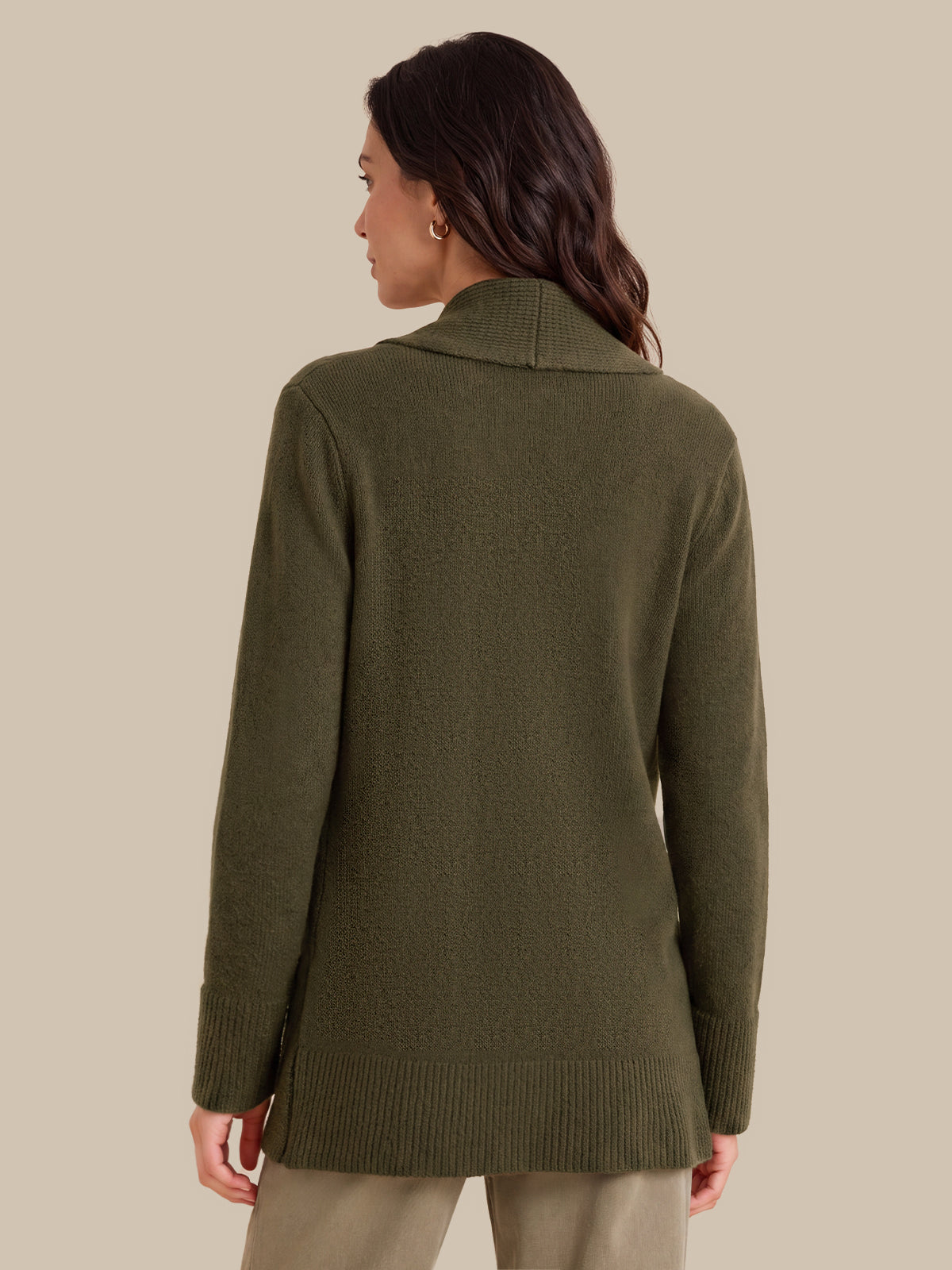 A woman shown from the back wearing an olive green knit sweater with a wide collar and ribbed cuffs and hem, paired with light beige pants, against a solid beige background.