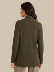 A woman shown from the back wearing an olive green knit sweater with a wide collar and ribbed cuffs and hem, paired with light beige pants, against a solid beige background.