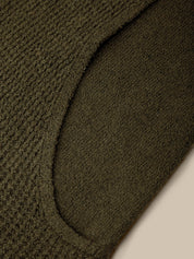 Close-up of a dark olive green knit fabric with a ribbed texture and a curved seam detail, set against a light beige background.