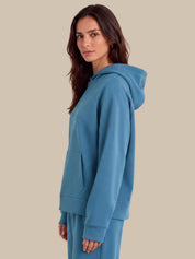A woman wearing a matching blue hoodie and sweatpants set, shown in side profile against a solid beige background.