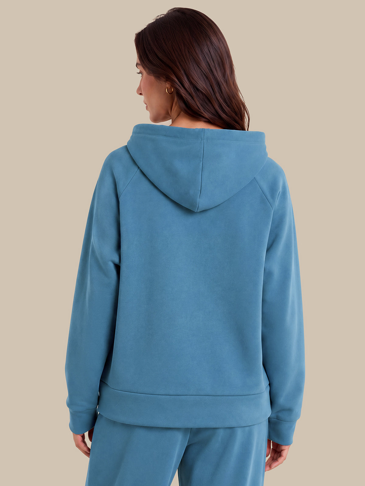 A woman shown from the back wearing a dusty blue hooded sweatshirt and matching sweatpants against a solid beige background.