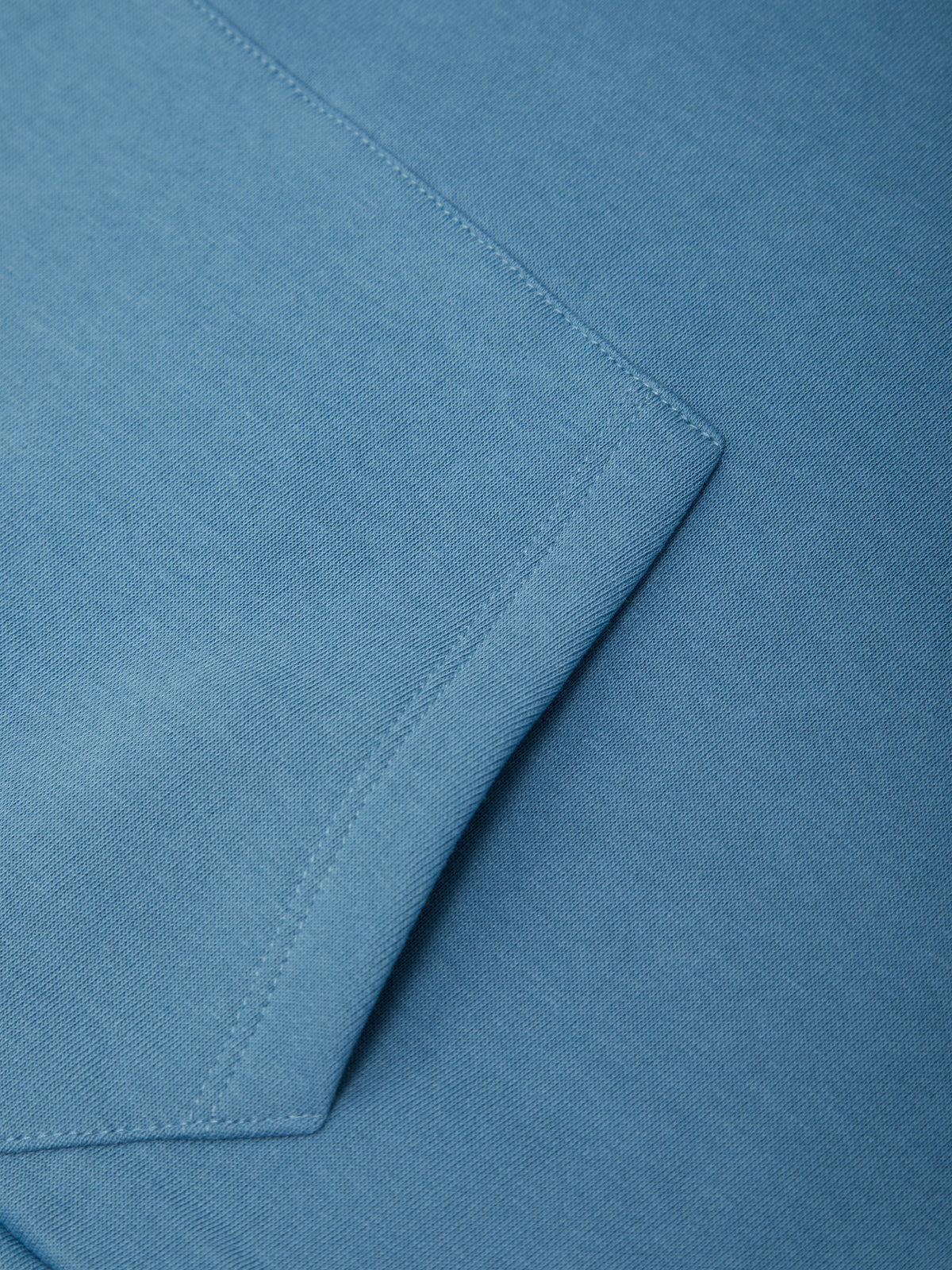 Close-up of a blue fabric surface with a folded corner showing fine woven texture and neat stitching.