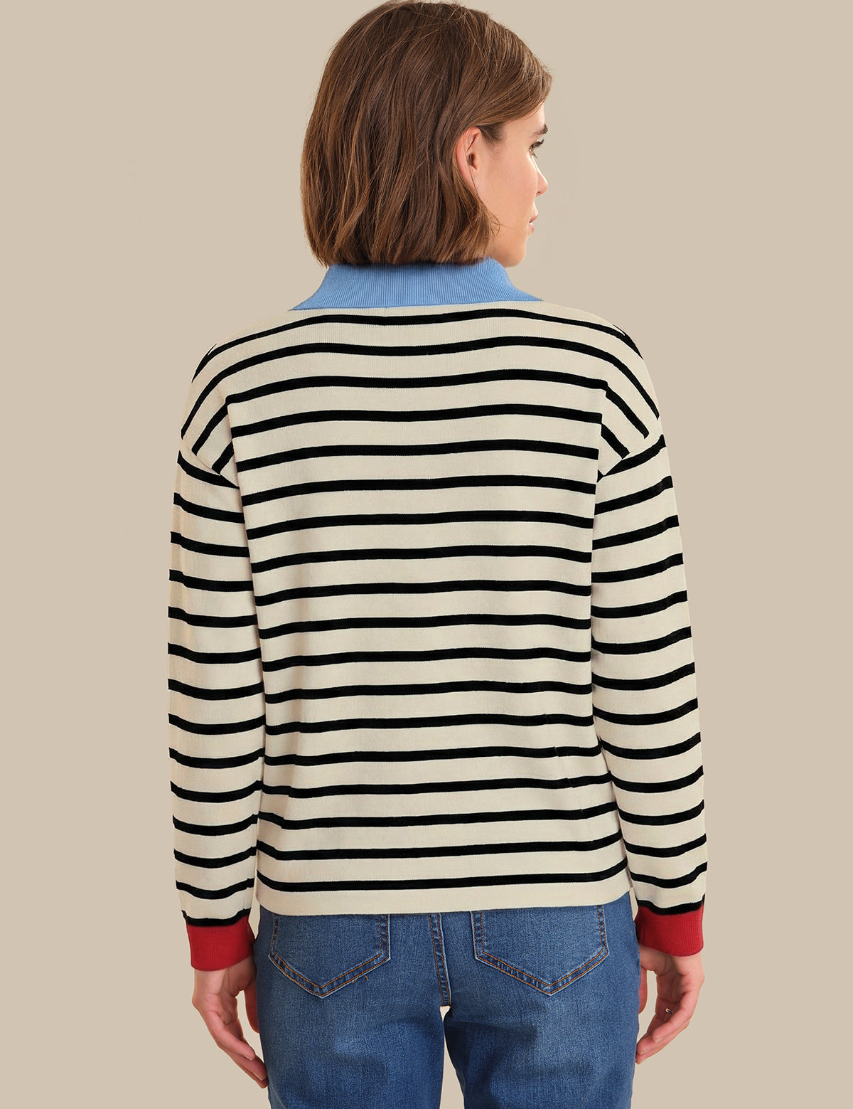 Person wearing a black and white striped sweater with red cuffs and hem on a beige background