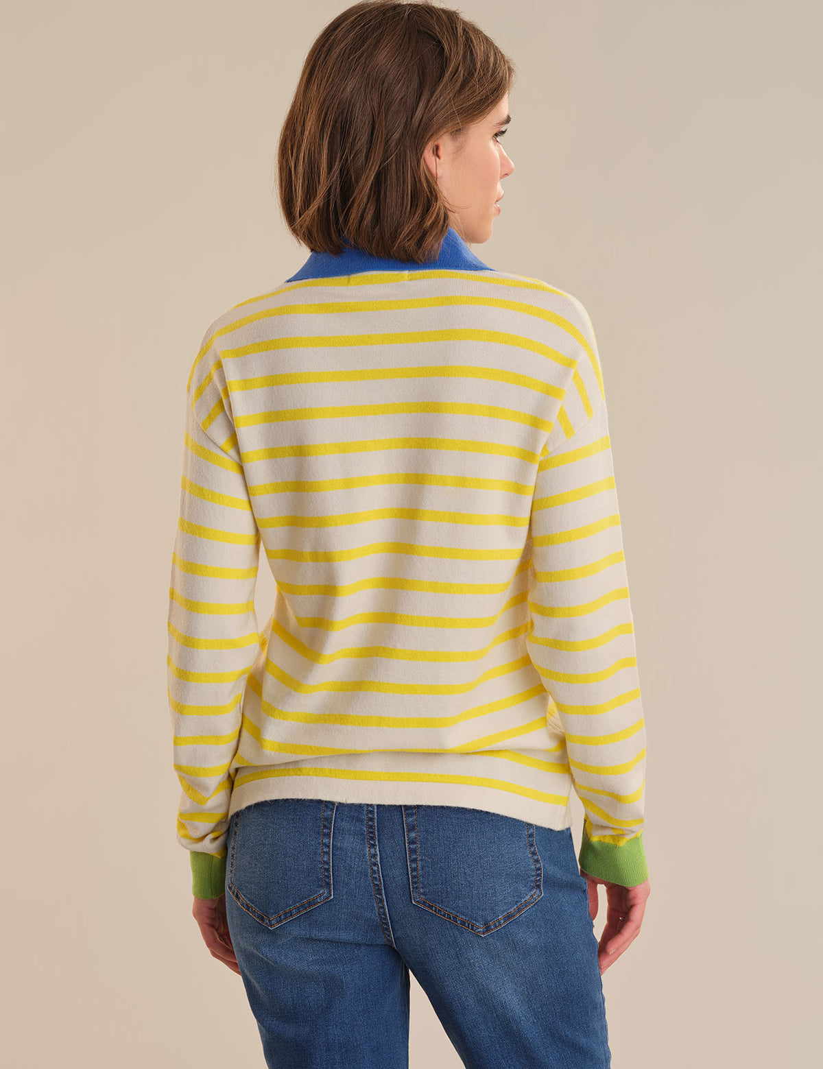 Person wearing a yellow and white striped sweater with blue jeans on a beige background