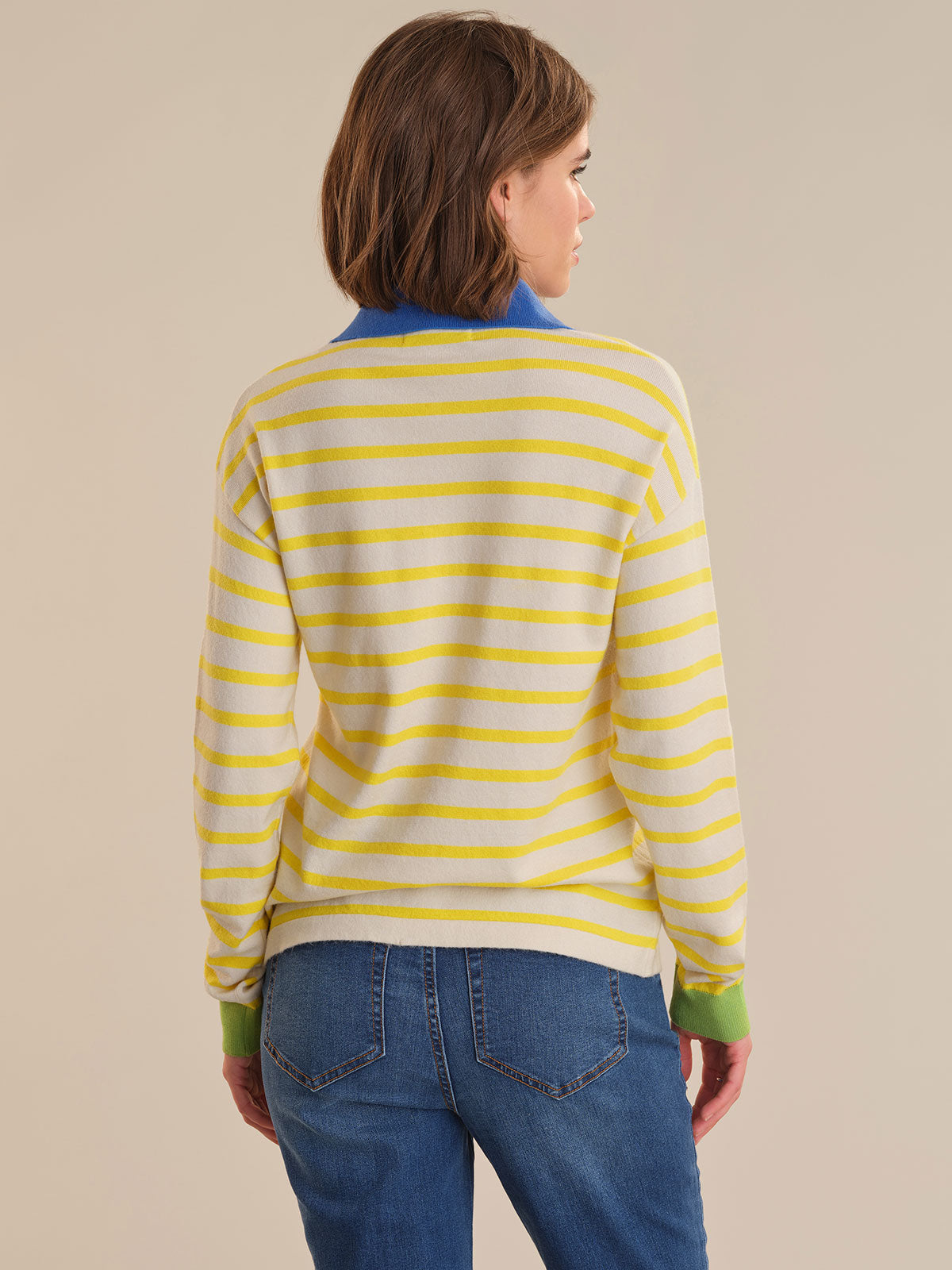 Person wearing a yellow and white striped sweater with blue jeans on a beige background