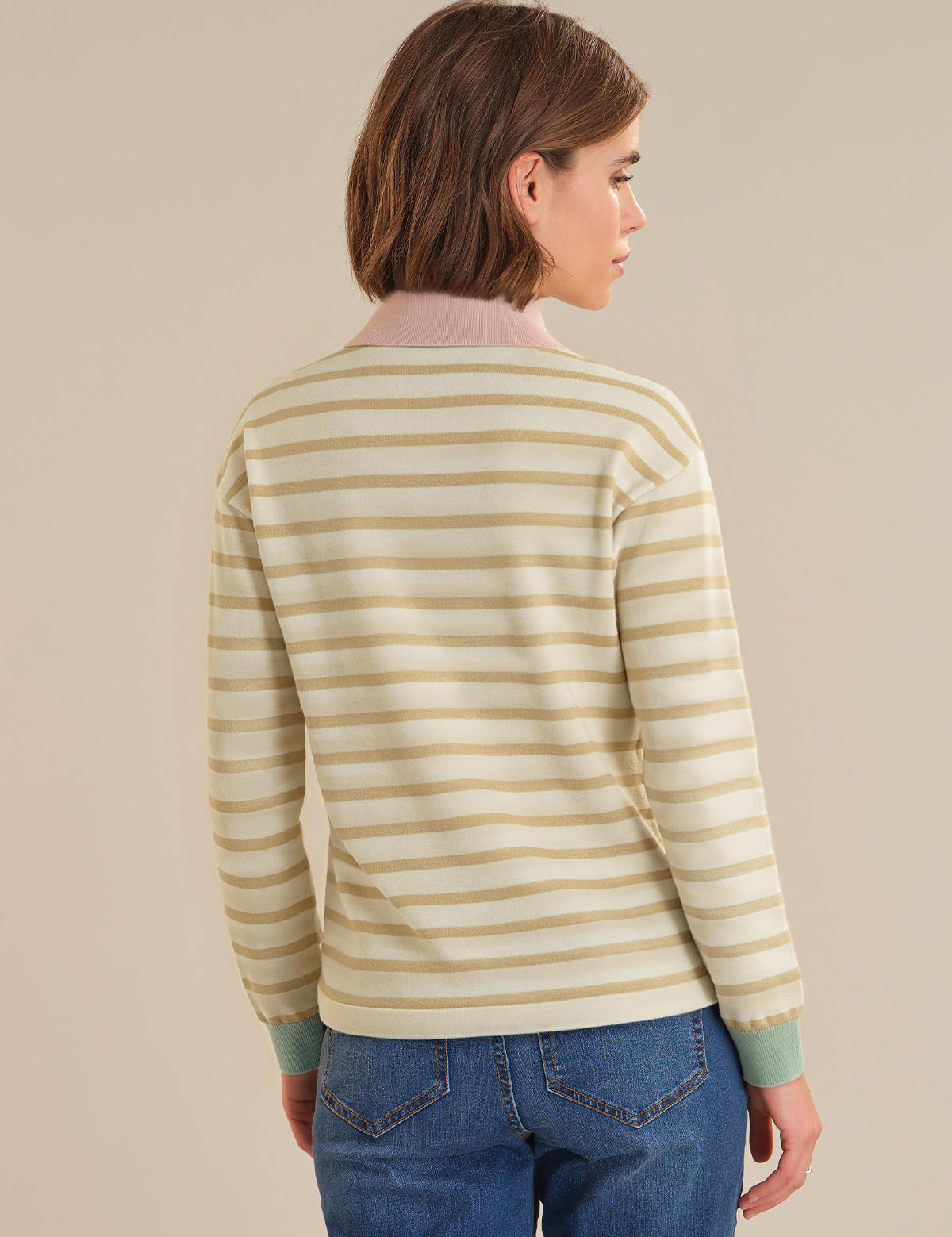 Person wearing a striped sweater and blue jeans against a beige background