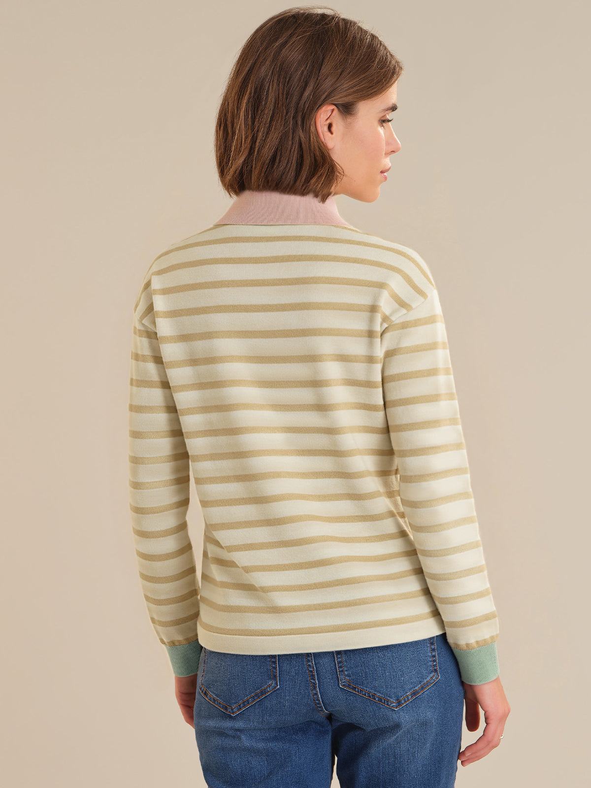 Person wearing a striped sweater and blue jeans against a beige background