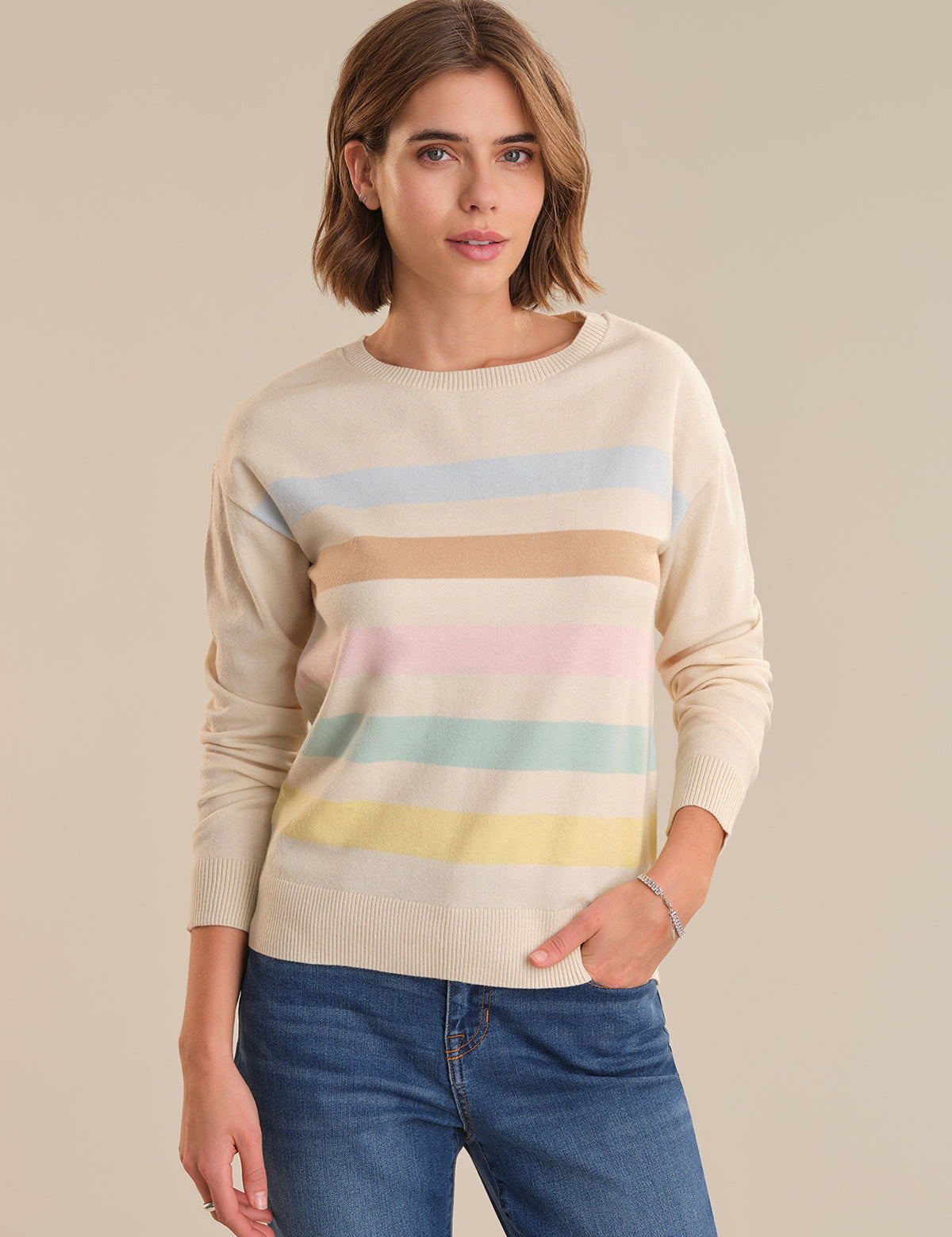 Woman wearing a beige sweater with colorful horizontal stripes on a beige background