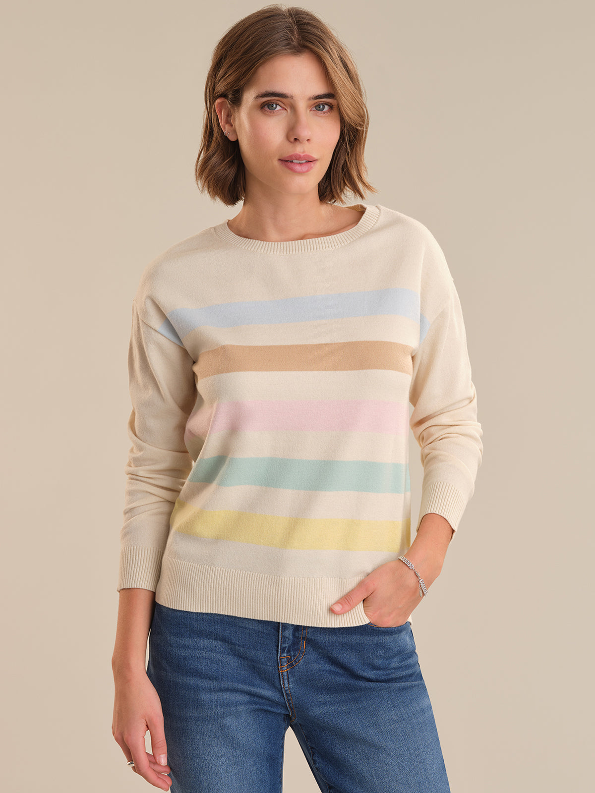 Woman wearing a beige sweater with colorful horizontal stripes on a beige background
