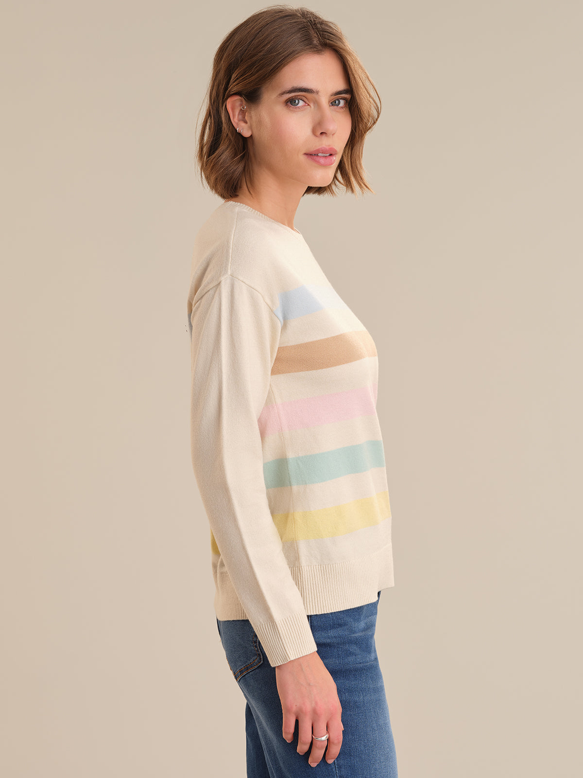 Woman wearing a cream sweater with colorful stripes on a beige background