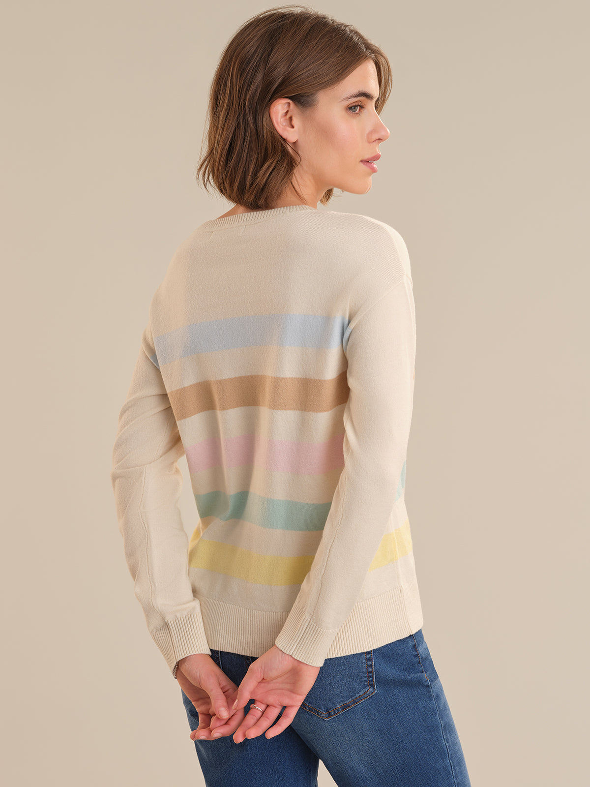 Woman wearing a beige sweater with colorful stripes on a plain background