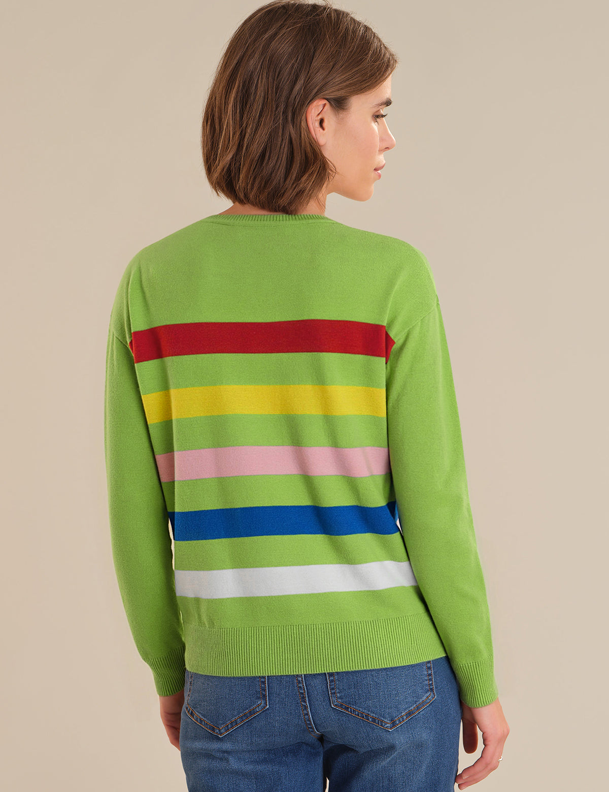 Person wearing a green sweater with colorful horizontal stripes on a beige background