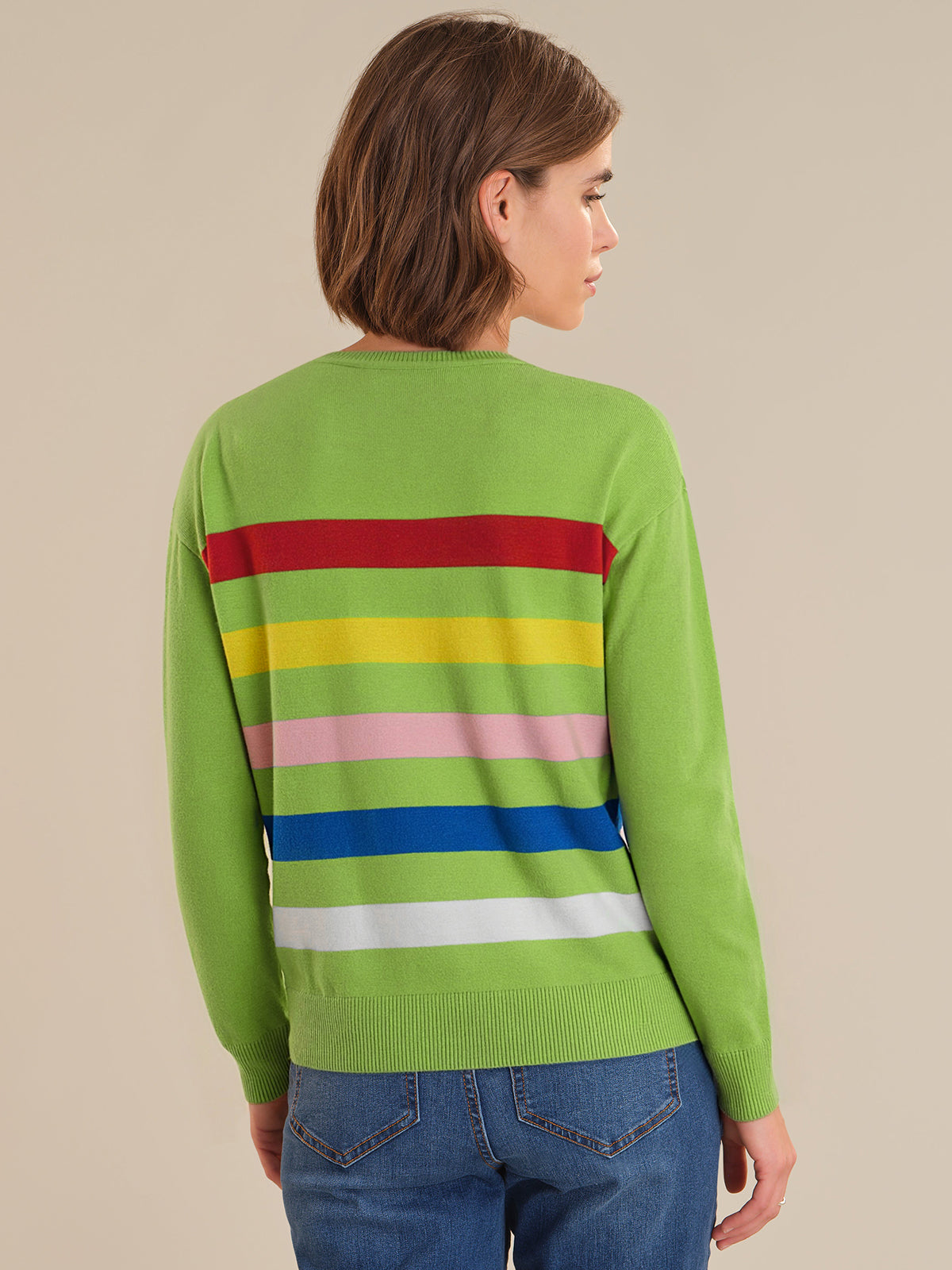 Person wearing a green sweater with colorful horizontal stripes on a beige background