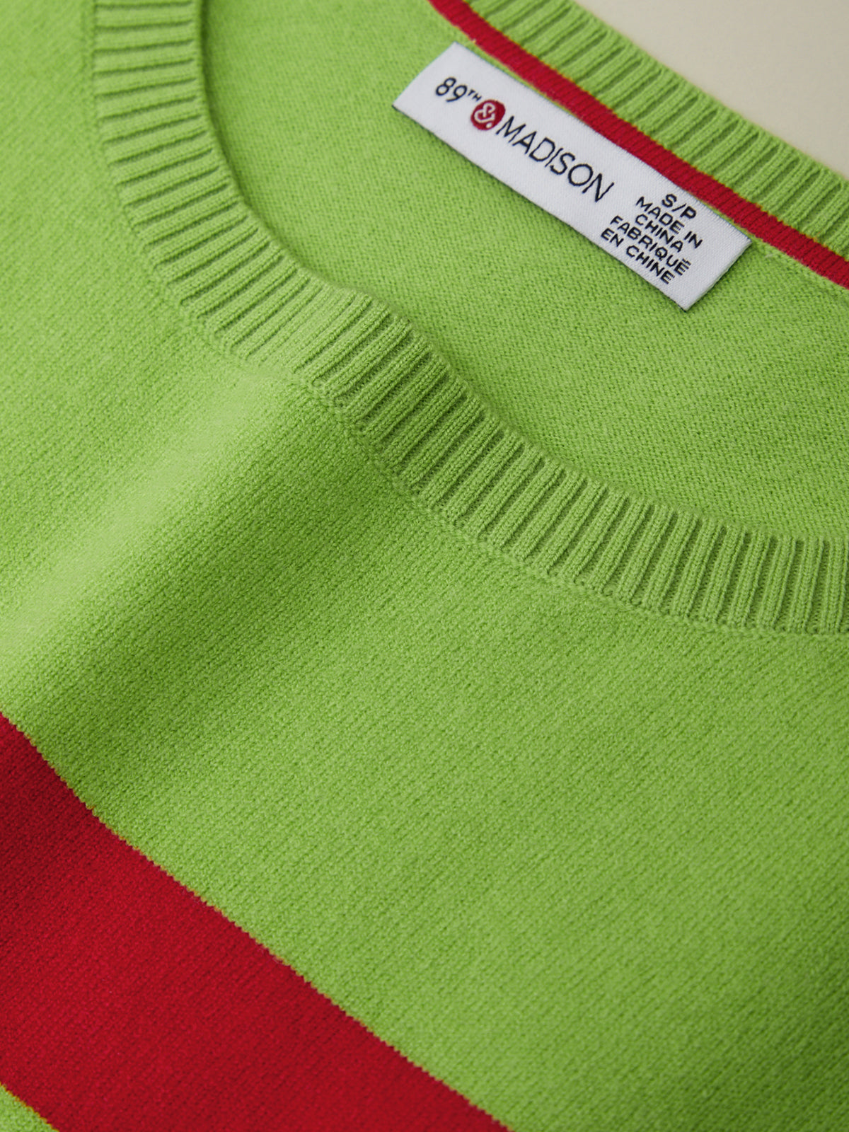 Close-up of a green sweater with a red stripe and a visible label.