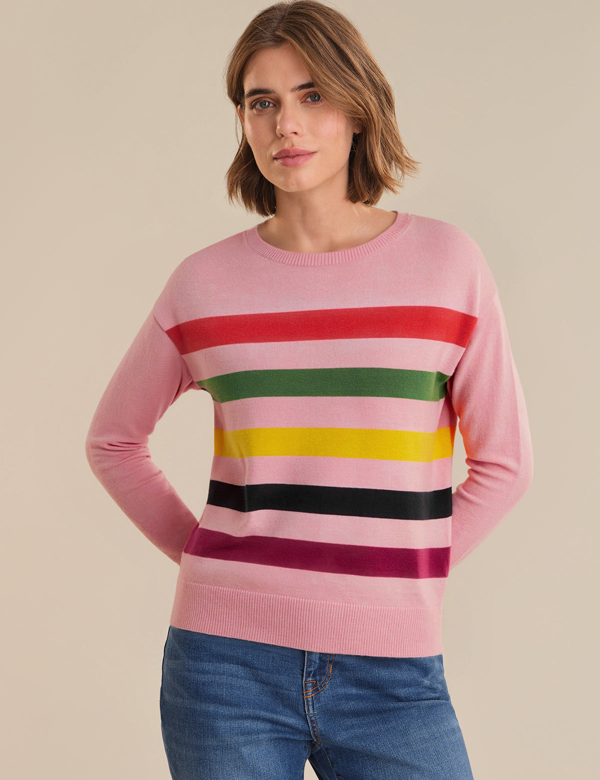 Woman wearing a pink sweater with colorful horizontal stripes on a beige background