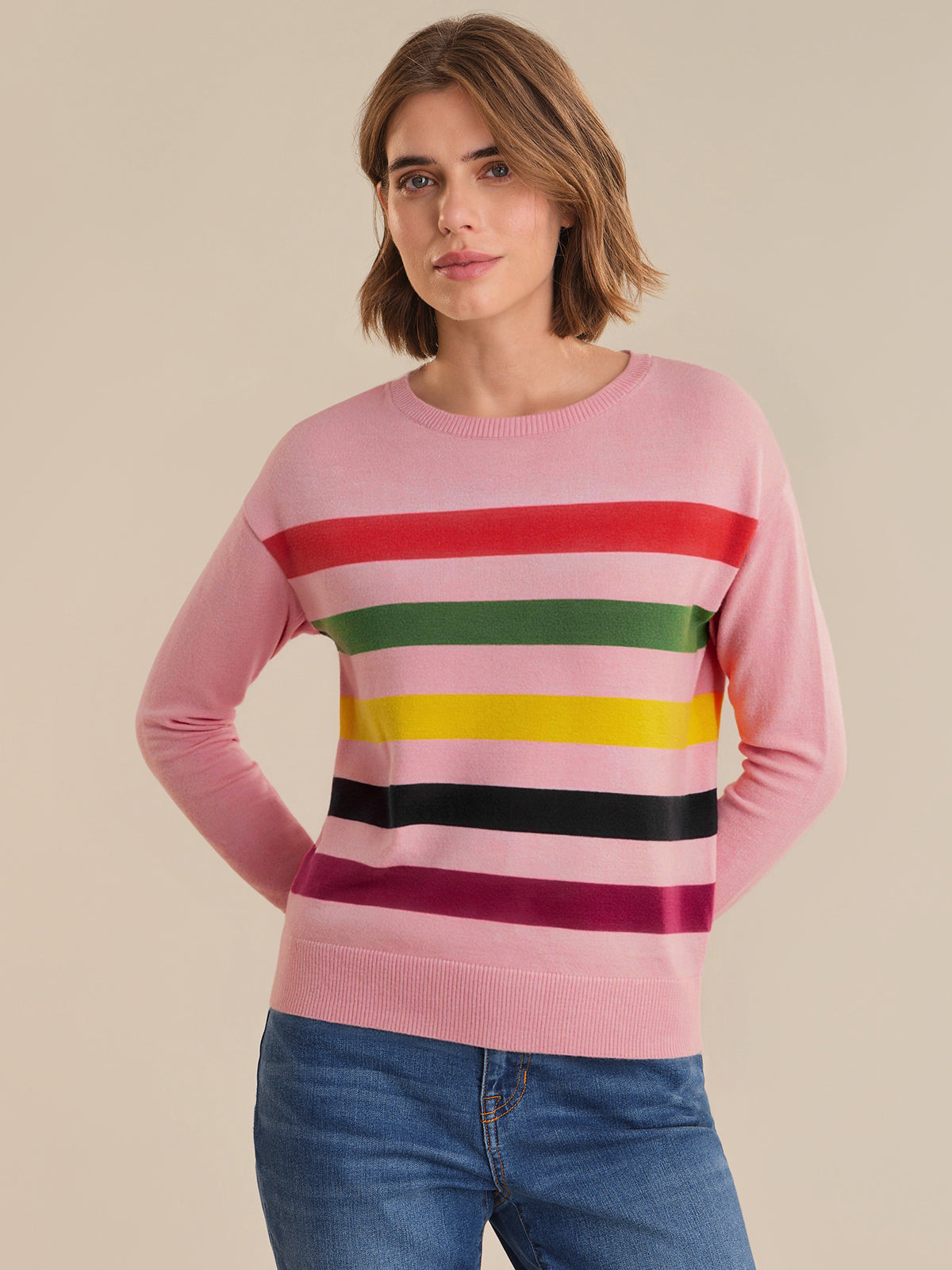 Woman wearing a pink sweater with colorful horizontal stripes on a beige background