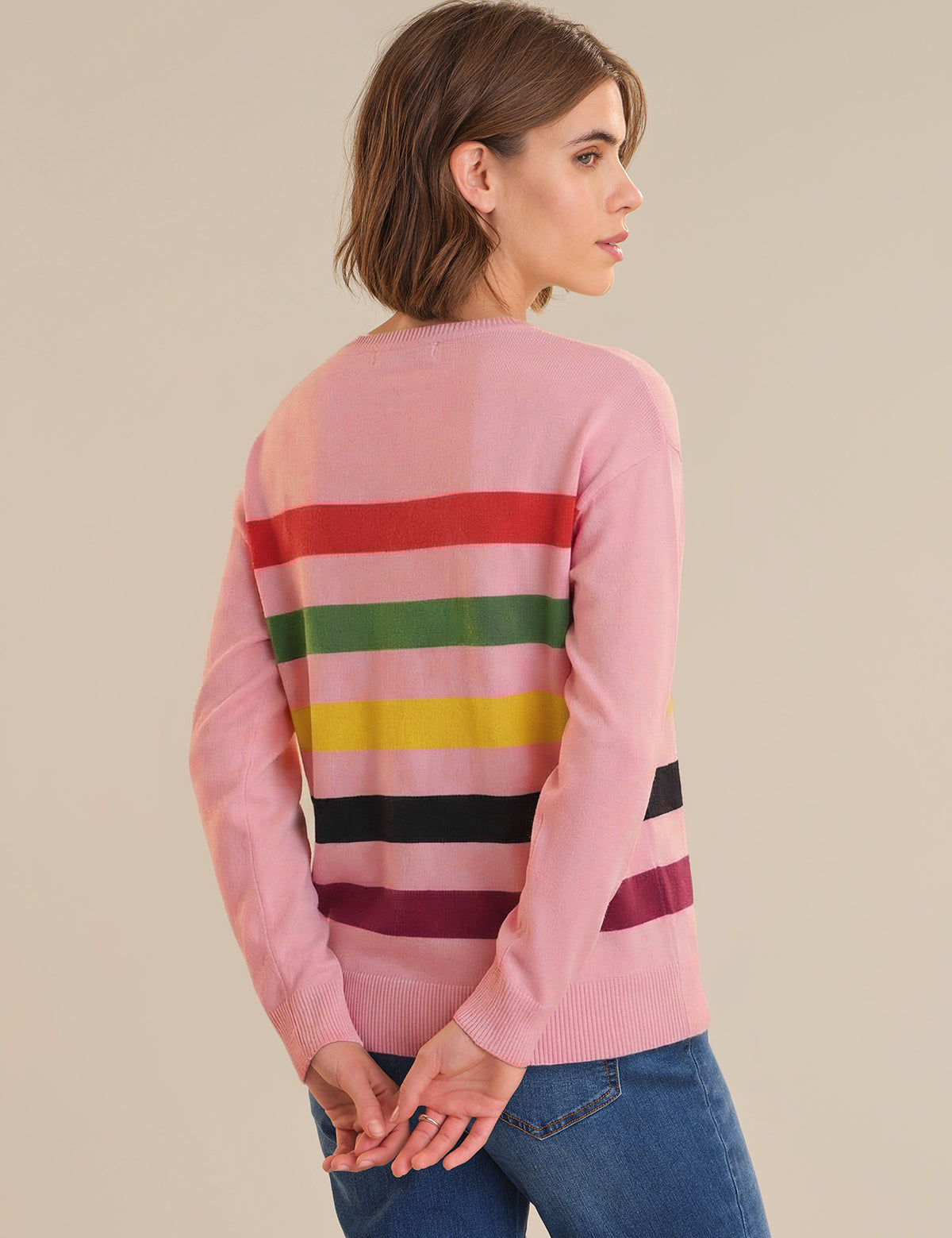 Woman wearing a pink sweater with colorful horizontal stripes on a beige background
