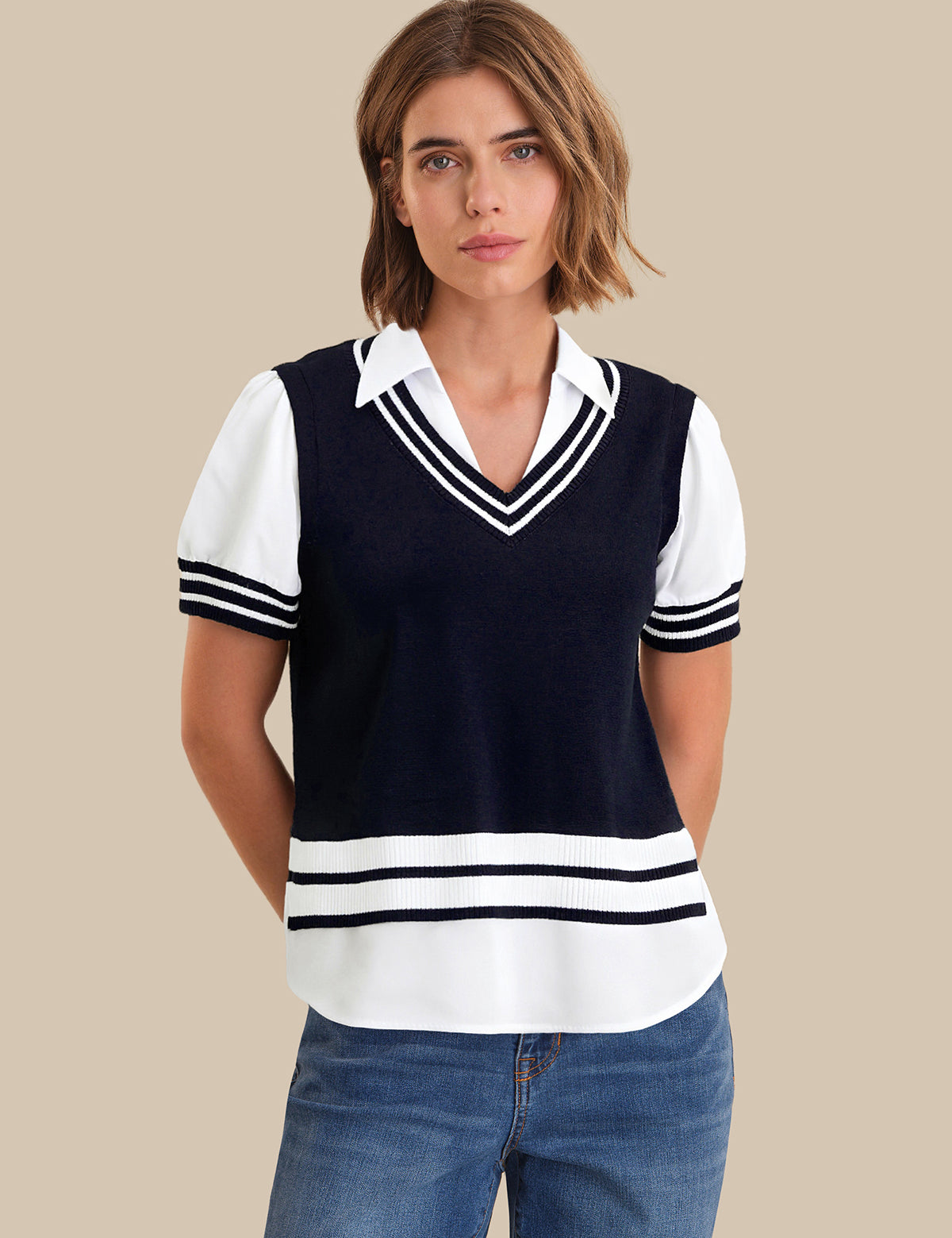 Woman wearing a navy and white striped sweater over a white shirt with blue jeans on a beige background