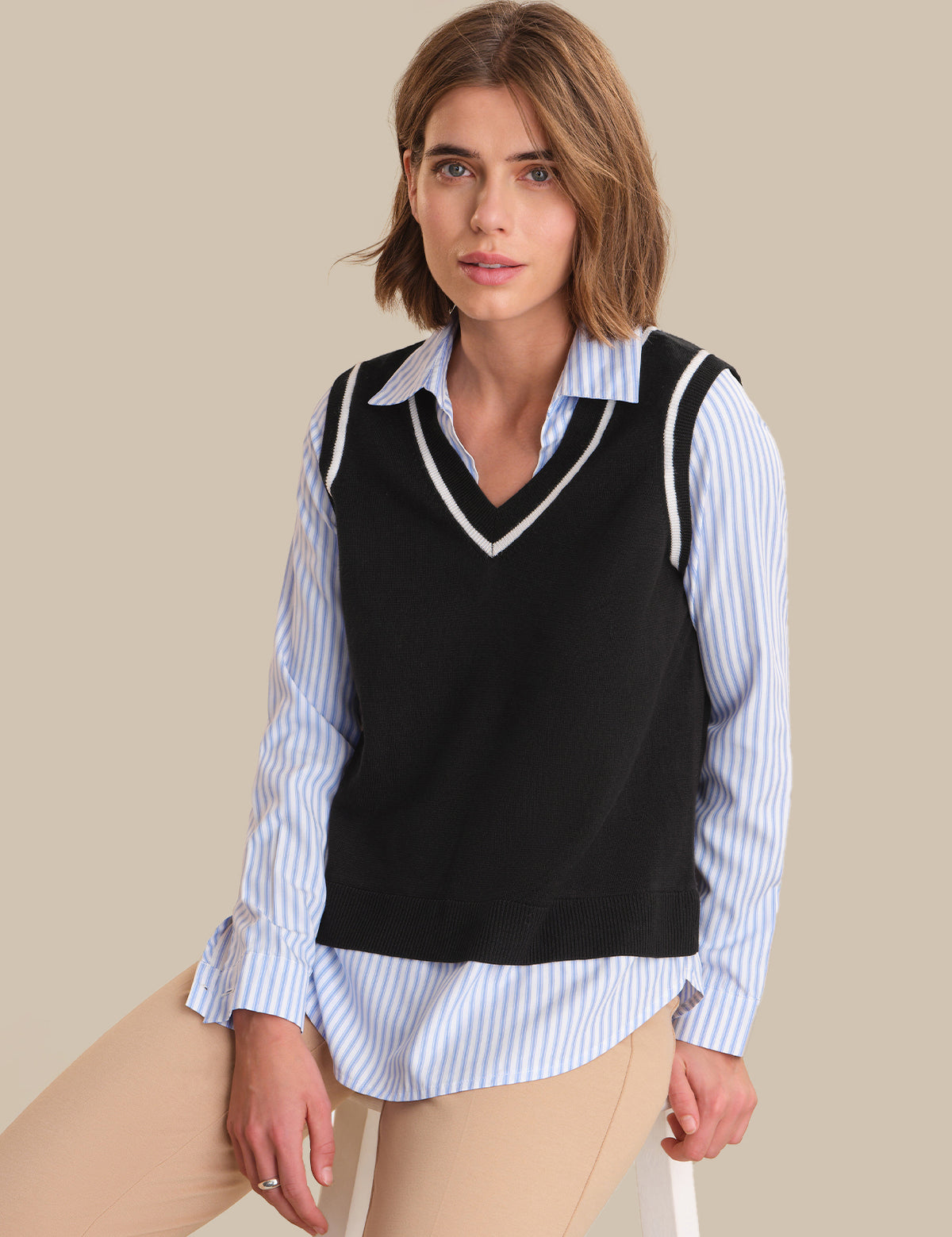Woman wearing a black vest over a striped shirt on a beige background