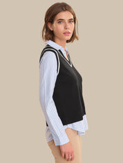 Woman wearing a black vest over a striped shirt on a beige background