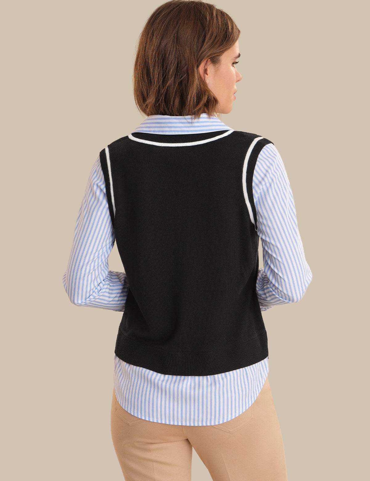 Woman wearing a black vest over a striped shirt on a beige background