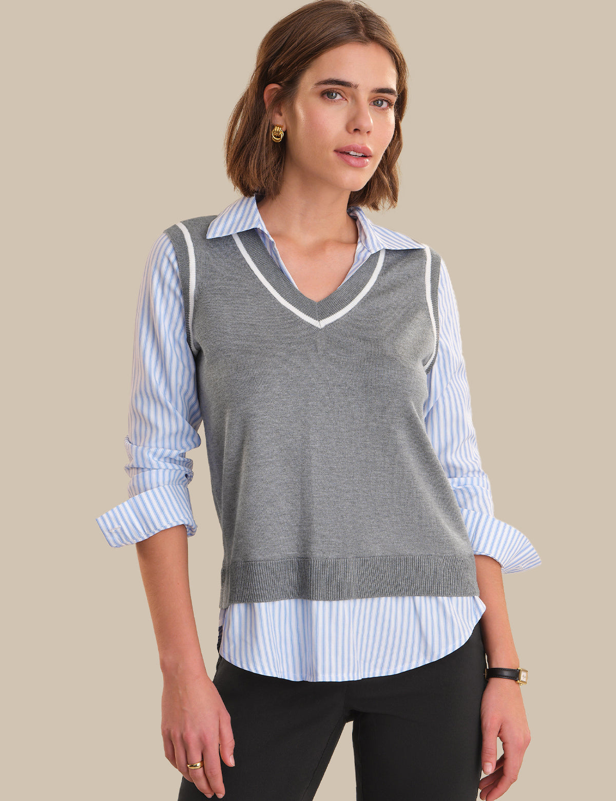 Woman wearing a gray sweater vest over a striped shirt on a beige background