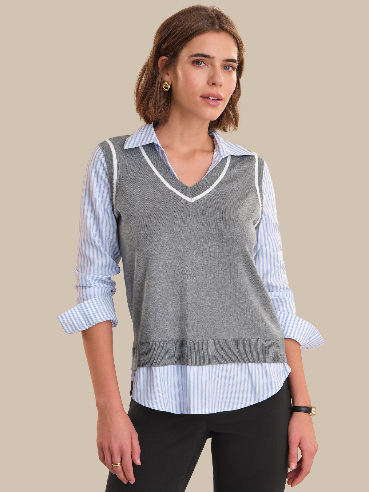 Woman wearing a gray sweater vest over a striped shirt on a beige background