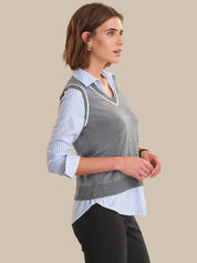 Woman wearing a gray vest over a striped shirt on a beige background