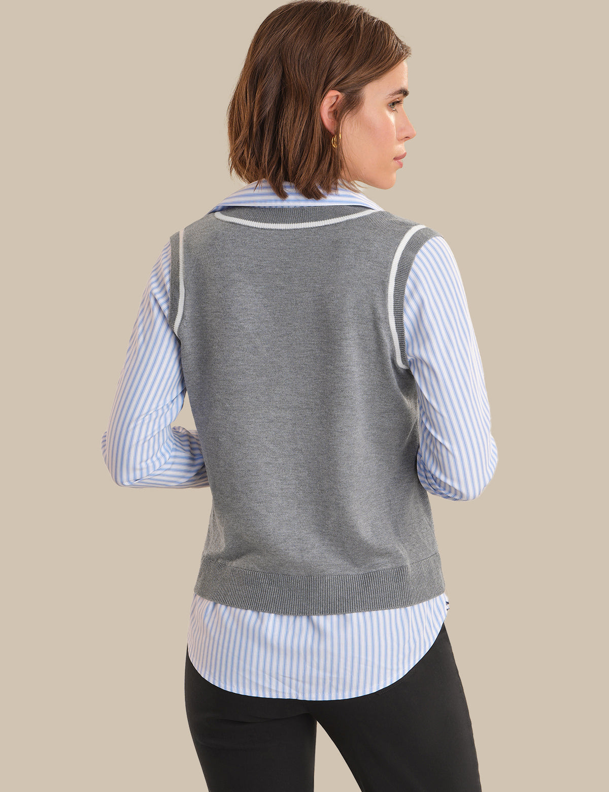Woman wearing a gray sweater vest over a striped shirt on a beige background