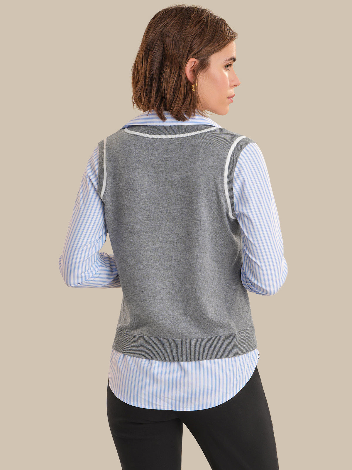 Woman wearing a gray sweater vest over a striped shirt on a beige background